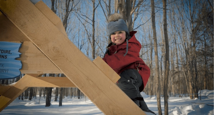 Enfant souriant grimpant une structure de bois en hiver.
