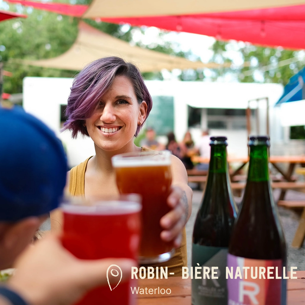 Personne souriante trinquant avec bière artisanale.